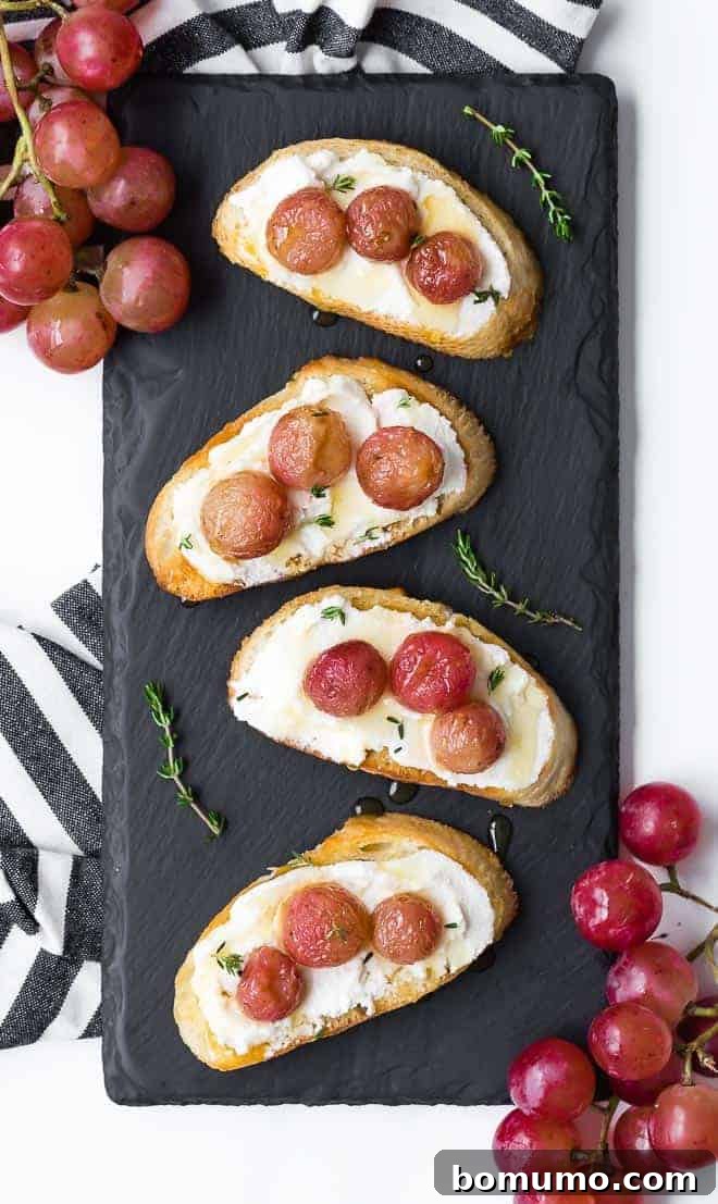 Image of four crostini on a small black slate board. Crostini is topped with roasted grapes and ricotta cheese.
