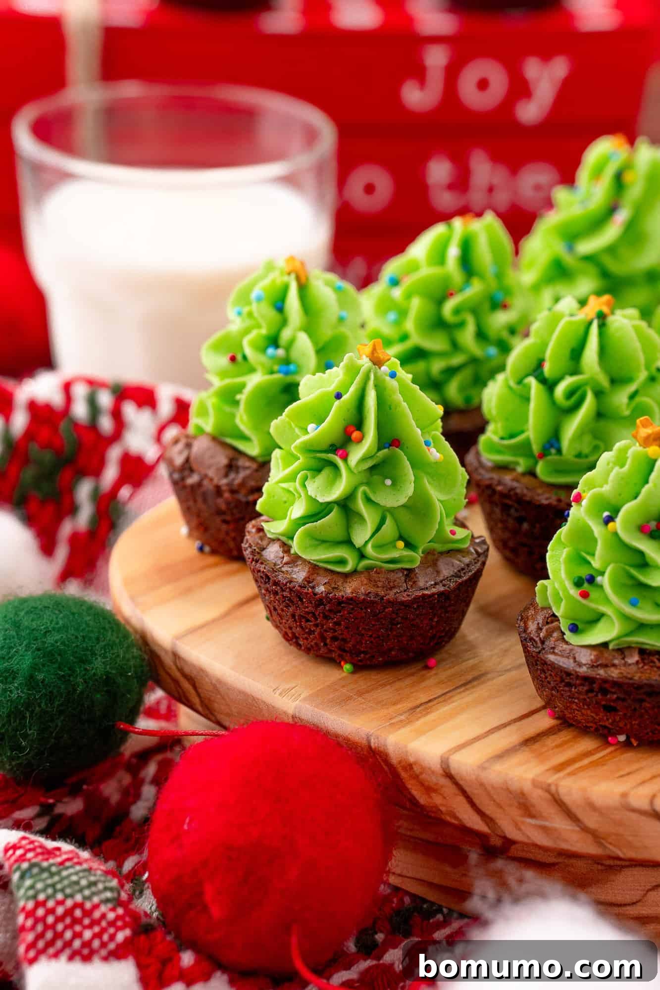 Mini brownies adorned with green frosting and sprinkles, designed to resemble festive Christmas trees, arranged on a holiday platter.