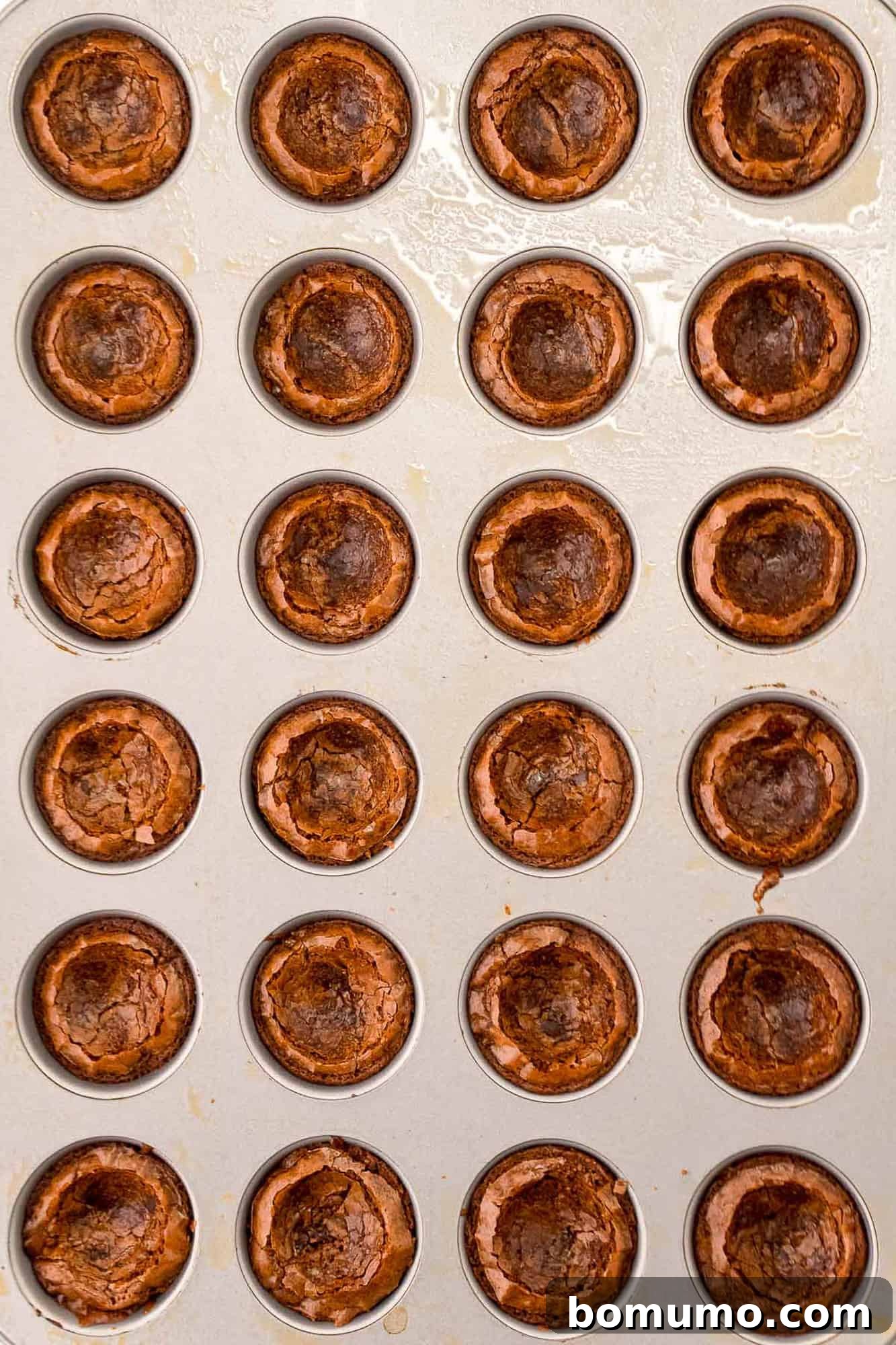 Mini brownies in a mini muffin pan, each with a carefully made indentation in its center, cooling down.