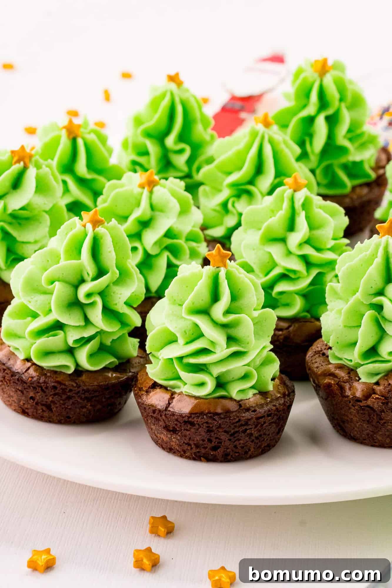 A collection of fully frosted and decorated brownie bites, artfully transformed into miniature Christmas trees, displayed on a serving tray.