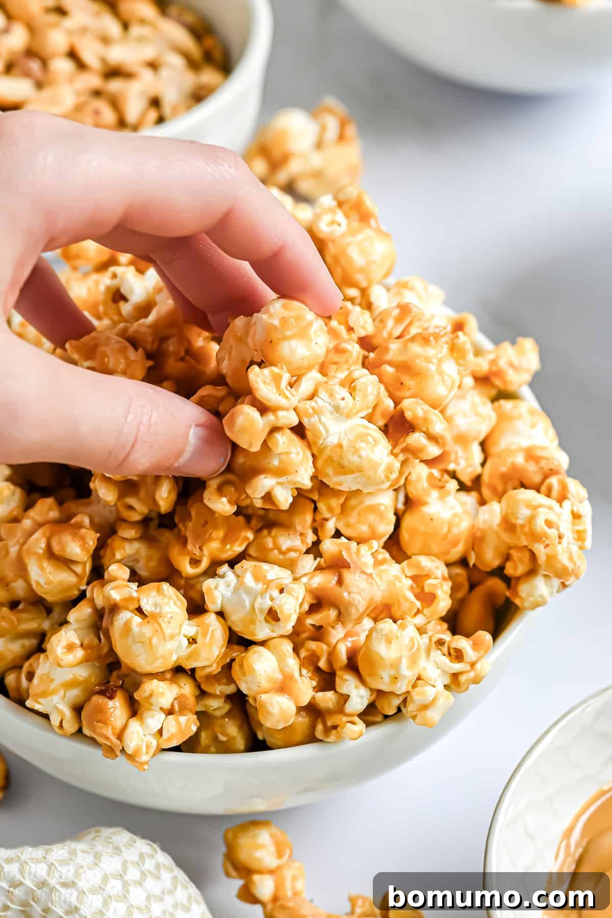 A hand reaching into a bowl to grab a handful of freshly made peanut butter popcorn.