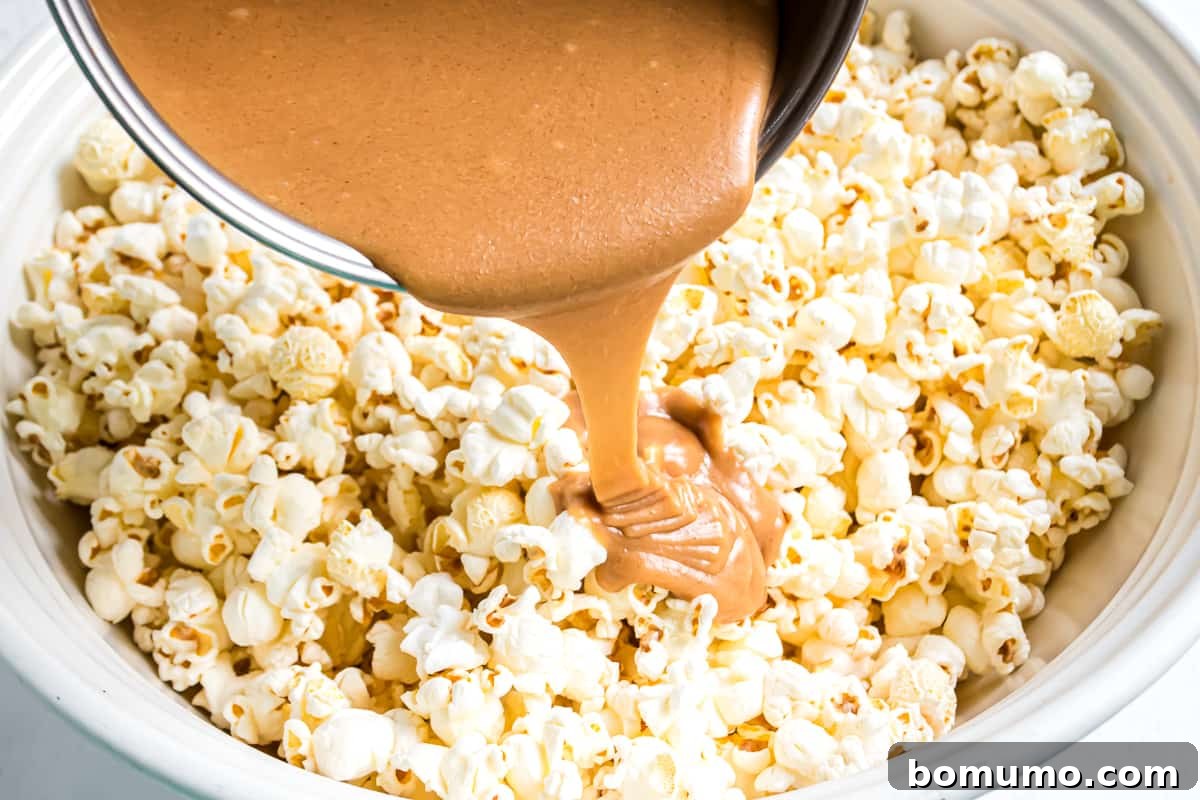 The warm peanut butter caramel being poured over the large bowl of popcorn and peanuts.