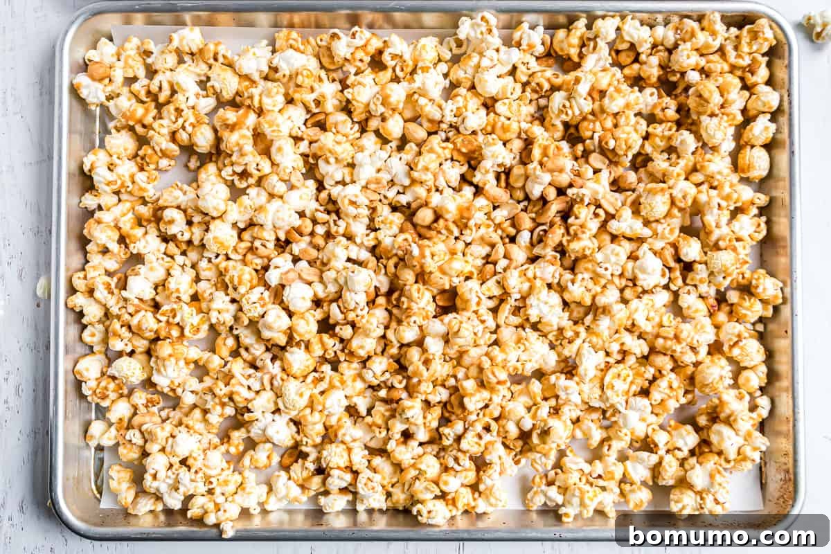 Peanut butter caramel popcorn spread out on a sheet pan, ready for baking.
