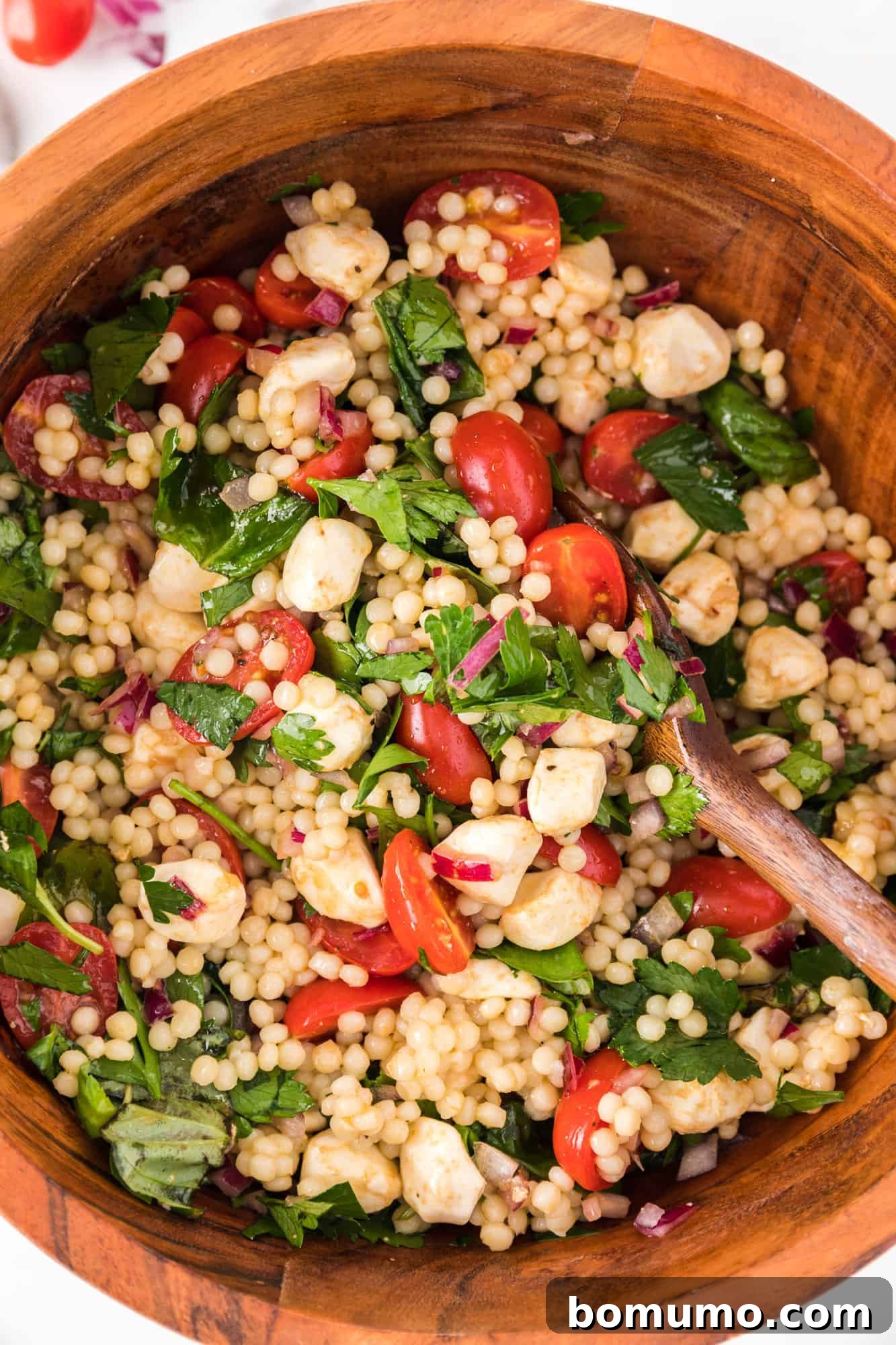 Couscous salad with herbs, tomatoes, mozzarella, in a large wooden bowl.