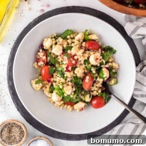 Israeli couscous salad with herbs and tomatoes in a large white bowl.