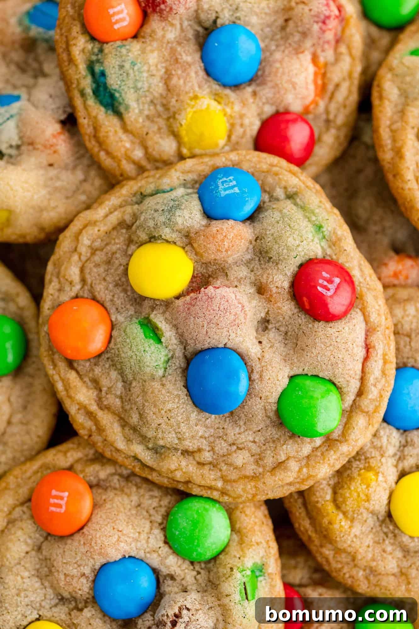 Ultimate M M Cookies 2 A stack of perfectly baked M&M cookies, with a single cookie prominently displayed on top, showcasing its vibrant candies.