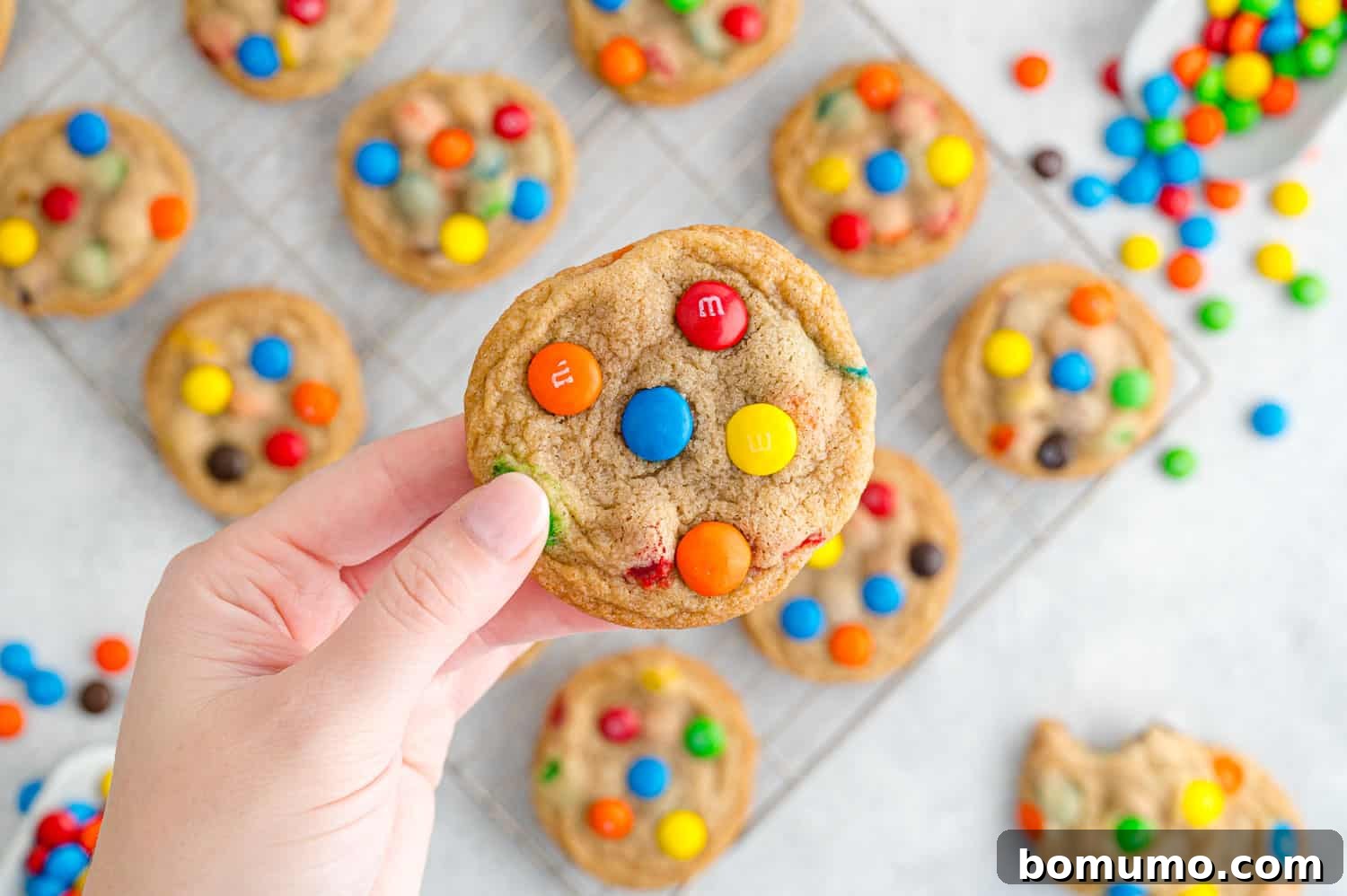 Ultimate M M Cookies 11 A warm, perfectly baked M&M cookie gently held in a hand, showcasing its soft texture and colorful candies.