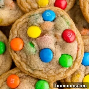 A delicious M&M cookie prominently displayed atop a pile of more colorful cookies.