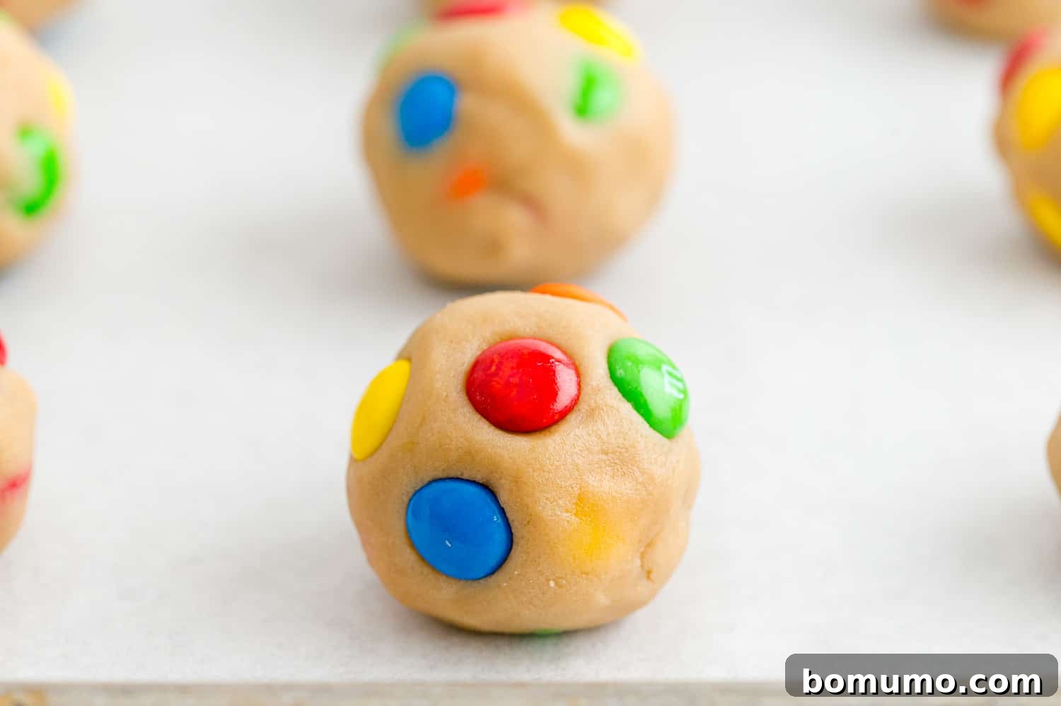Ultimate M M Cookies 10 Unbaked M&M cookie dough balls neatly arranged on a parchment-lined baking sheet, awaiting their transformation.