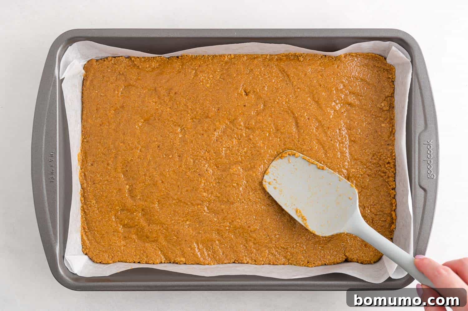 Peanut butter layer being pressed firmly into the prepared baking pan.