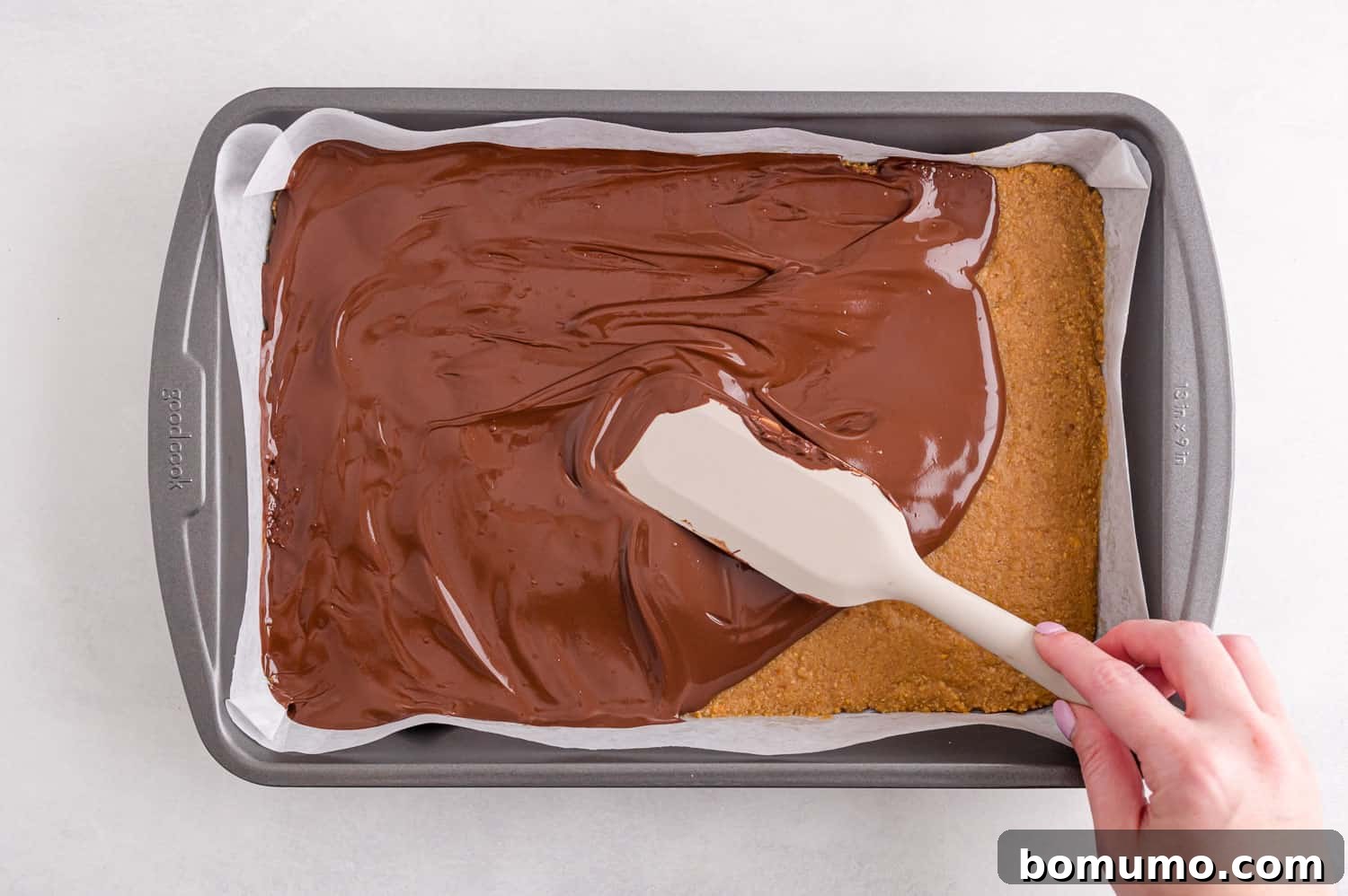 Smooth chocolate layer being poured and spread over the chilled peanut butter base.
