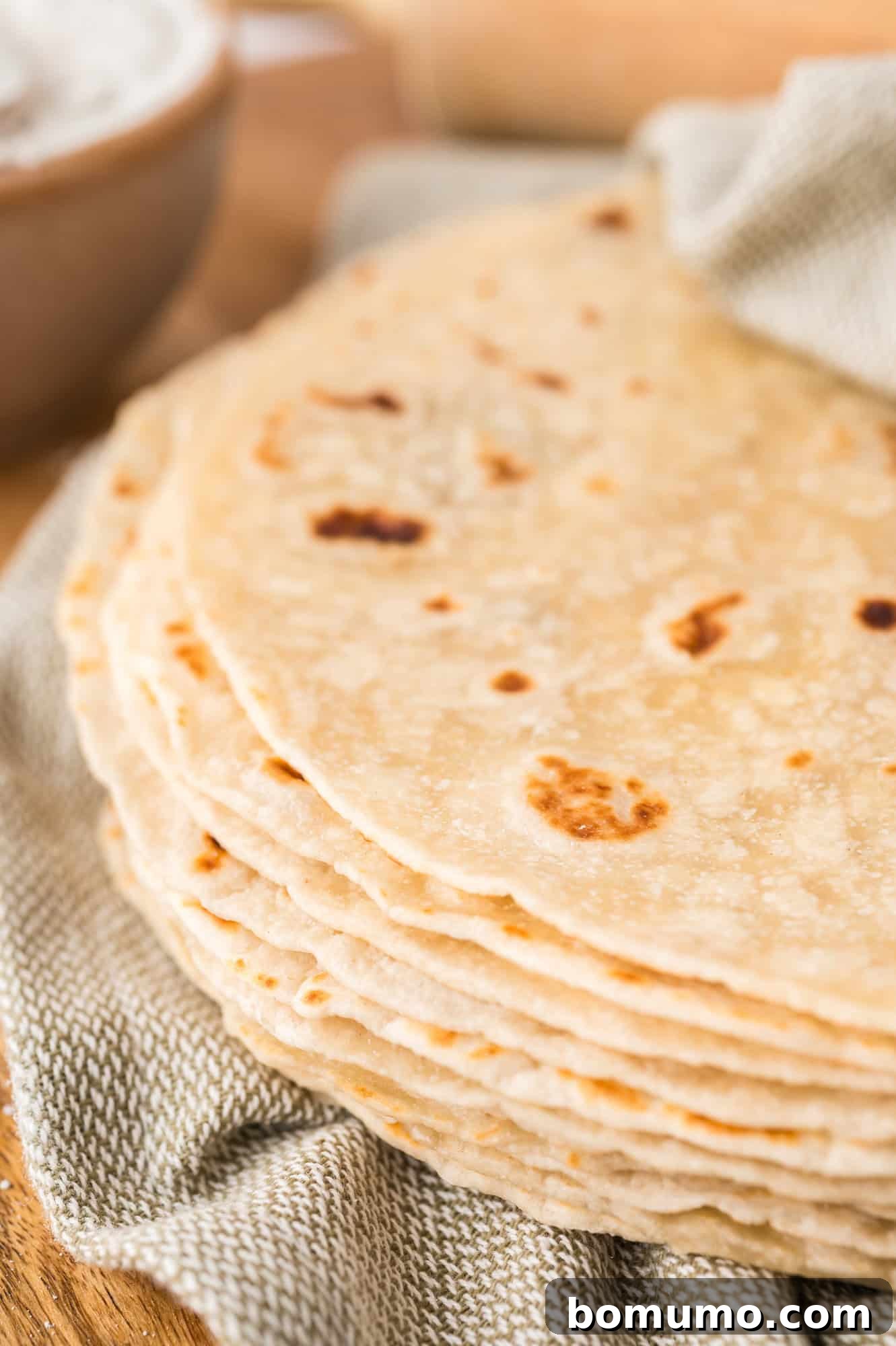 Stack of homemade tortillas partially wrapped in a light green linen cloth, exuding warmth and freshness.