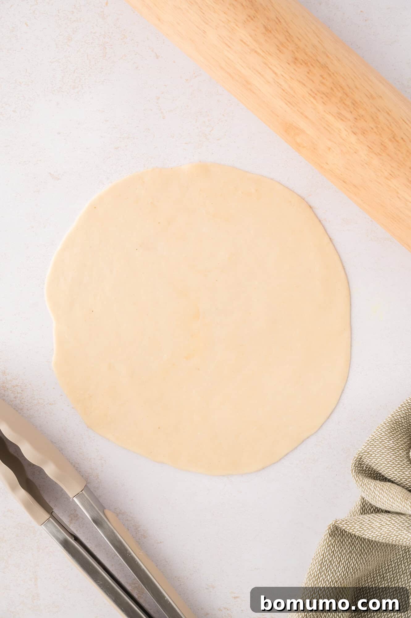 A tortilla dough ball rolled out thinly into a large, round circle on a surface.