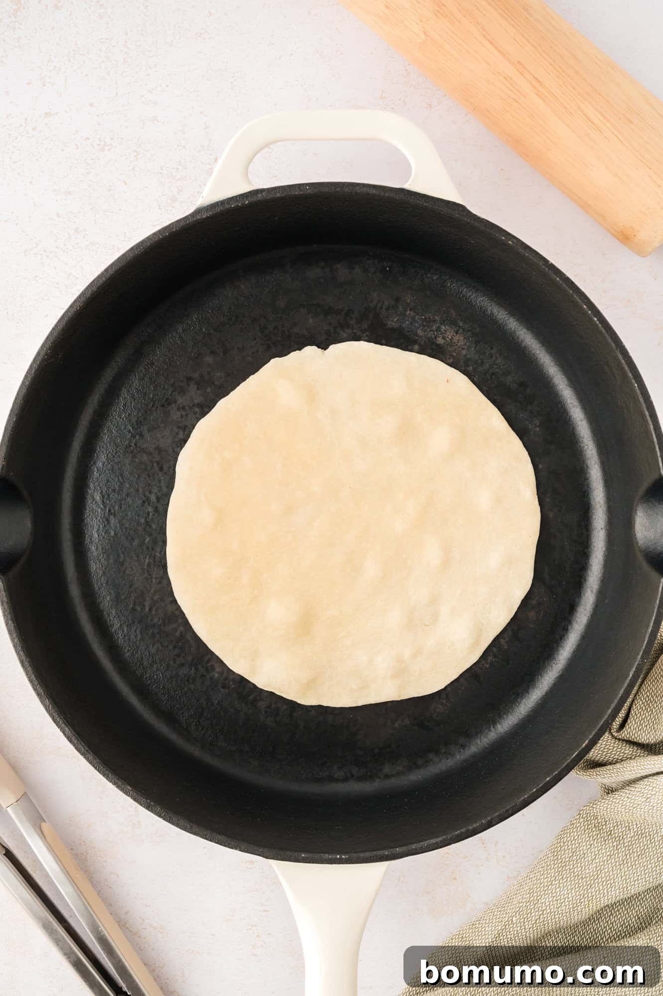 A single tortilla placed in a hot cast iron pan, just beginning to cook.