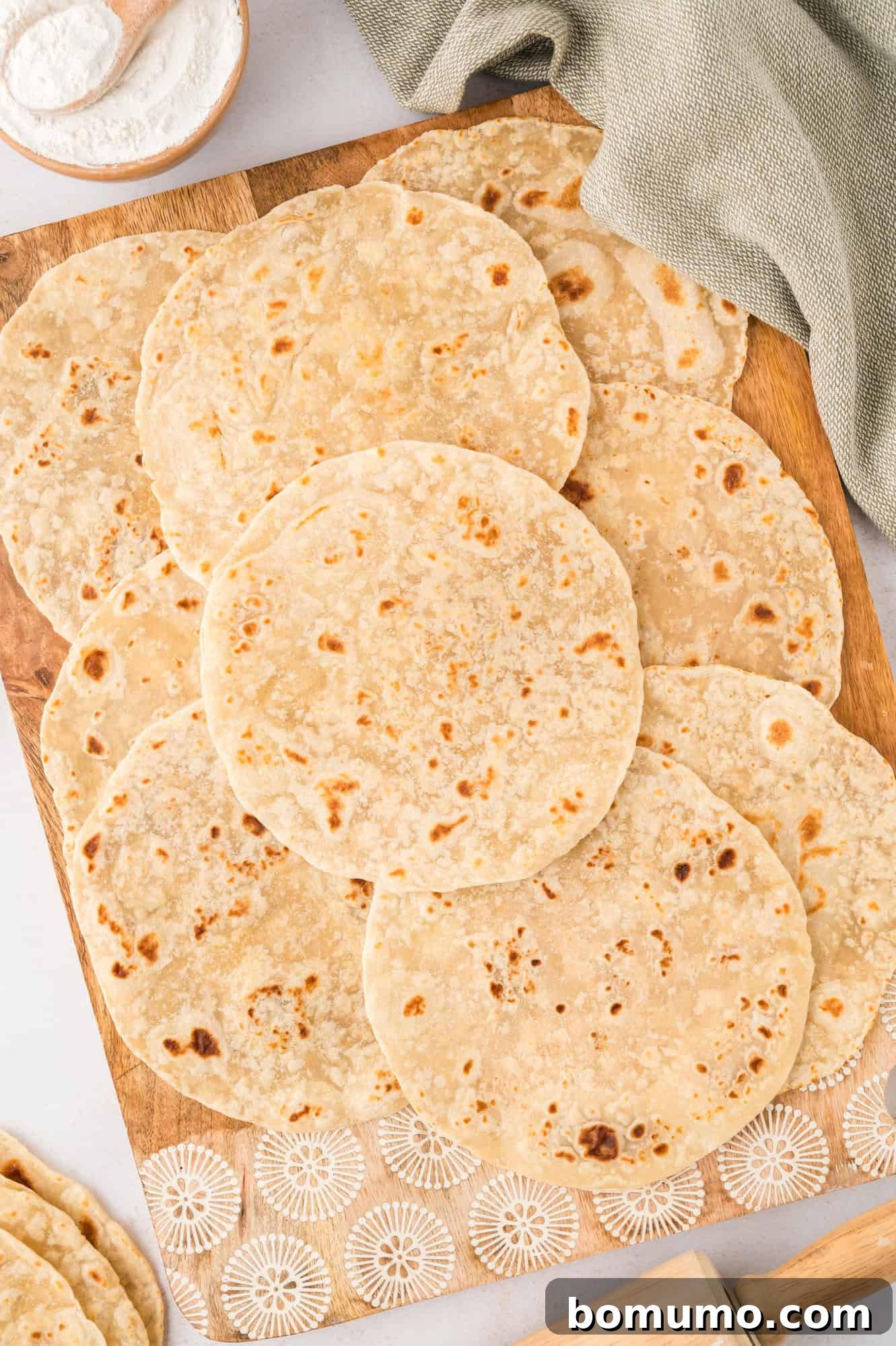 Freshly cooked tortillas laid out on a wooden cutting board, ready to be served.
