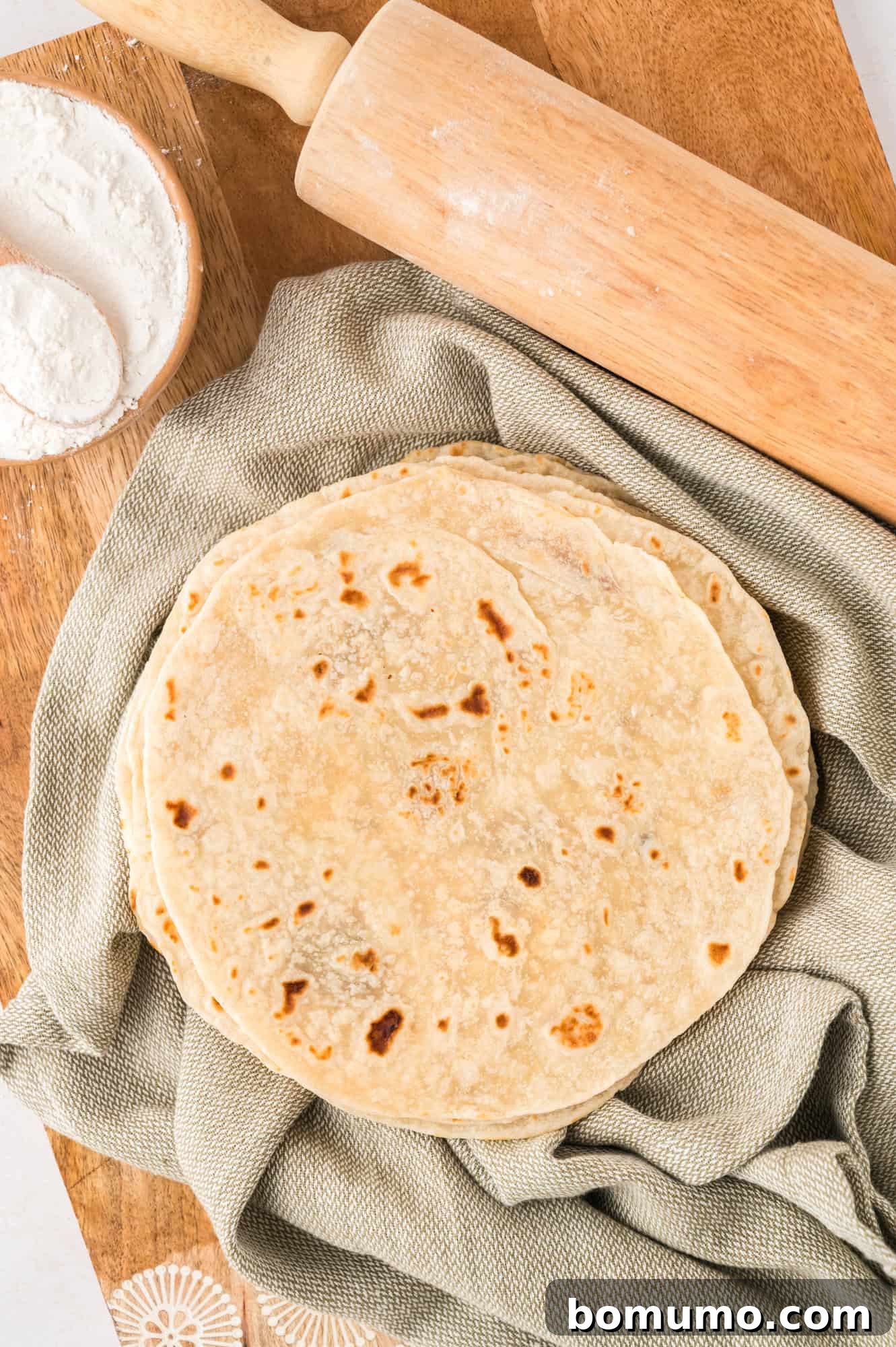 Overhead view of several homemade flour tortillas resting on a light green linen cloth.