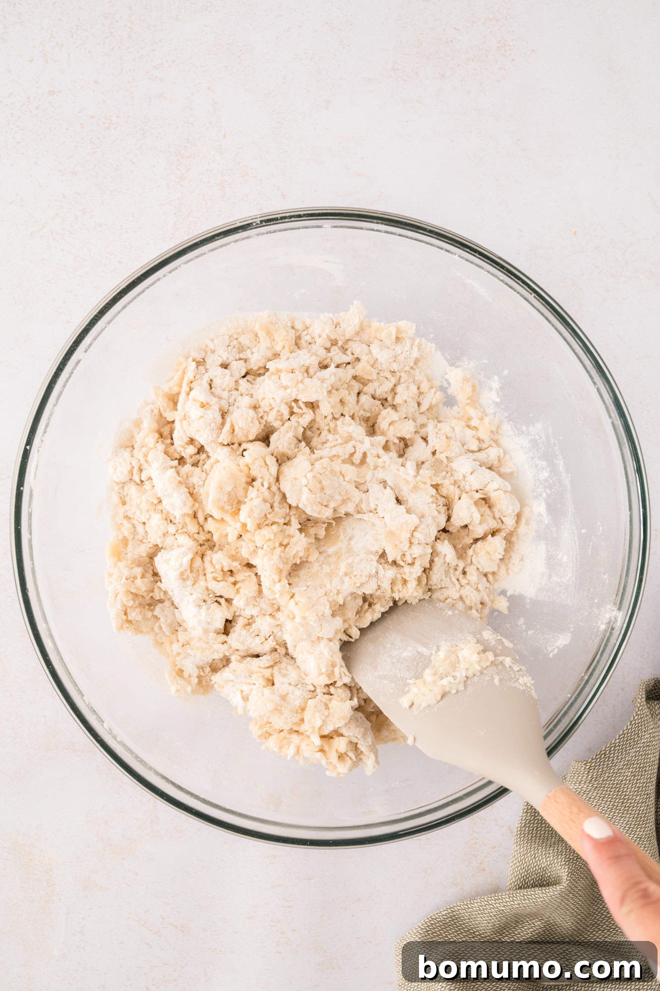 Tortilla dough starting to come together and being stirred with a spatula in a mixing bowl.