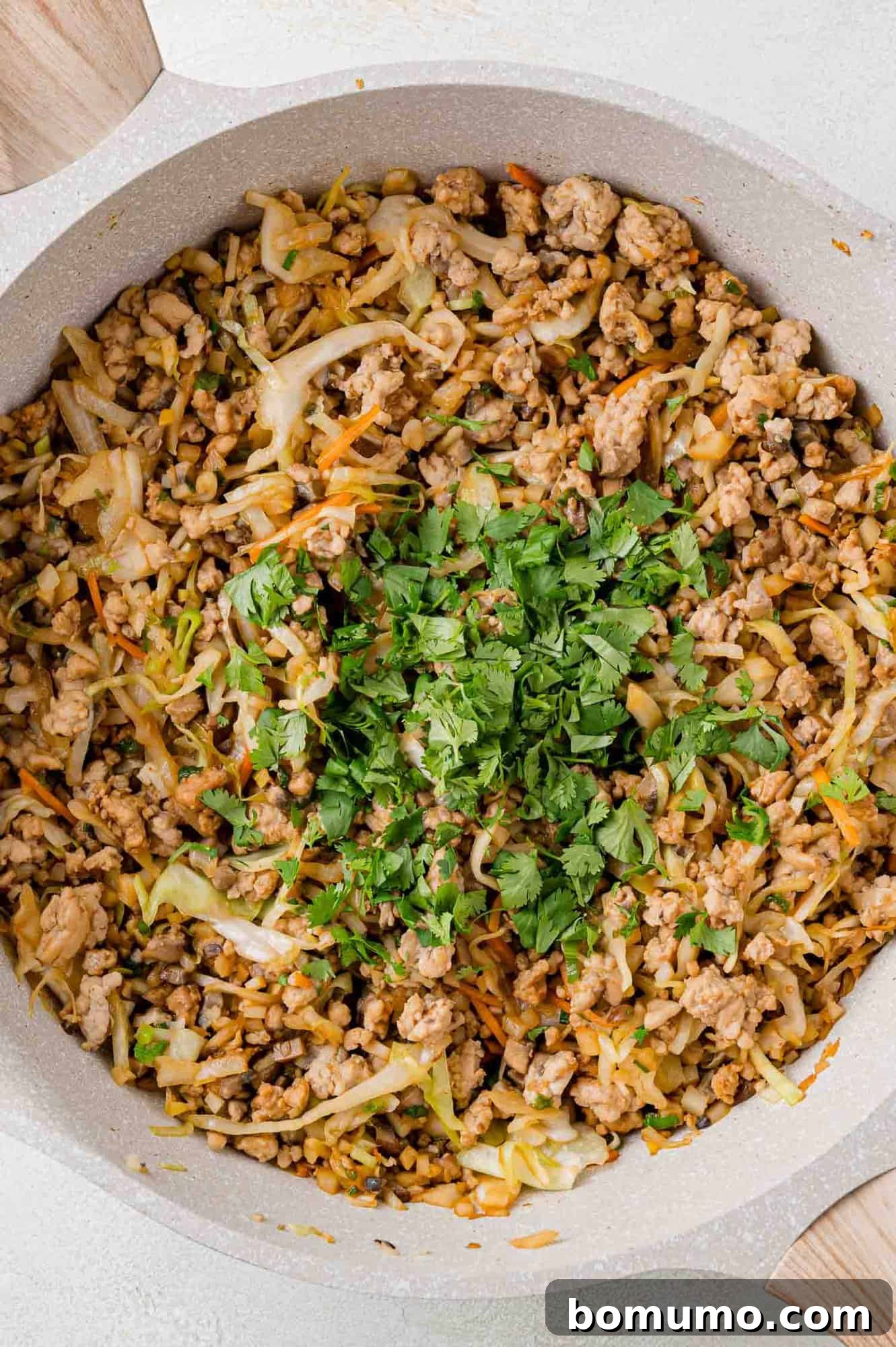 A skillet filled with seasoned ground meat, shredded cabbage, carrots, and topped with fresh chopped cilantro.