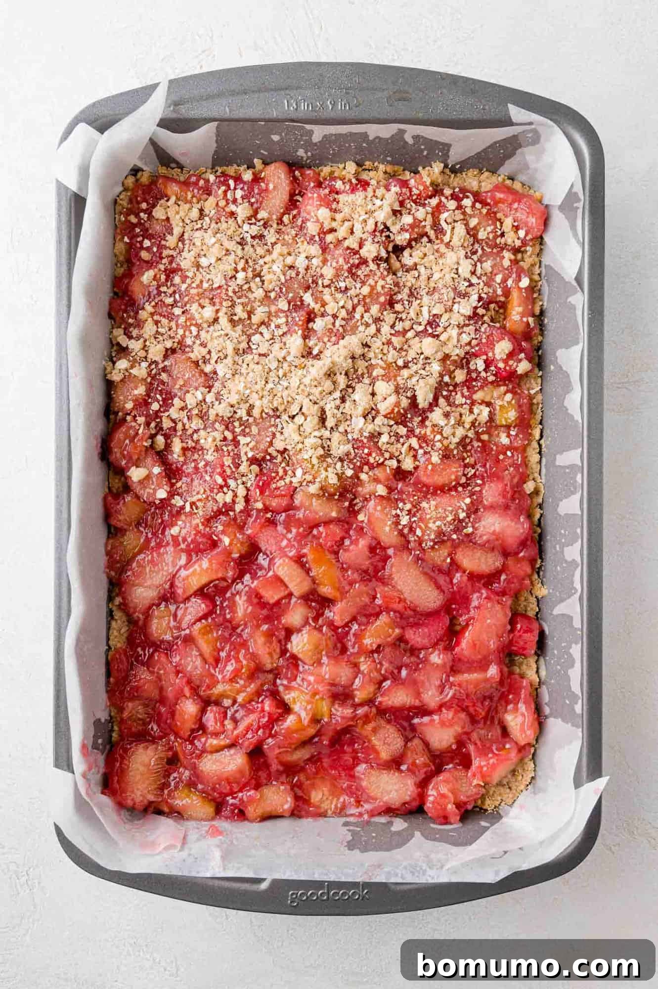 The final crumb topping being sprinkled and gently pressed over the rhubarb filling.