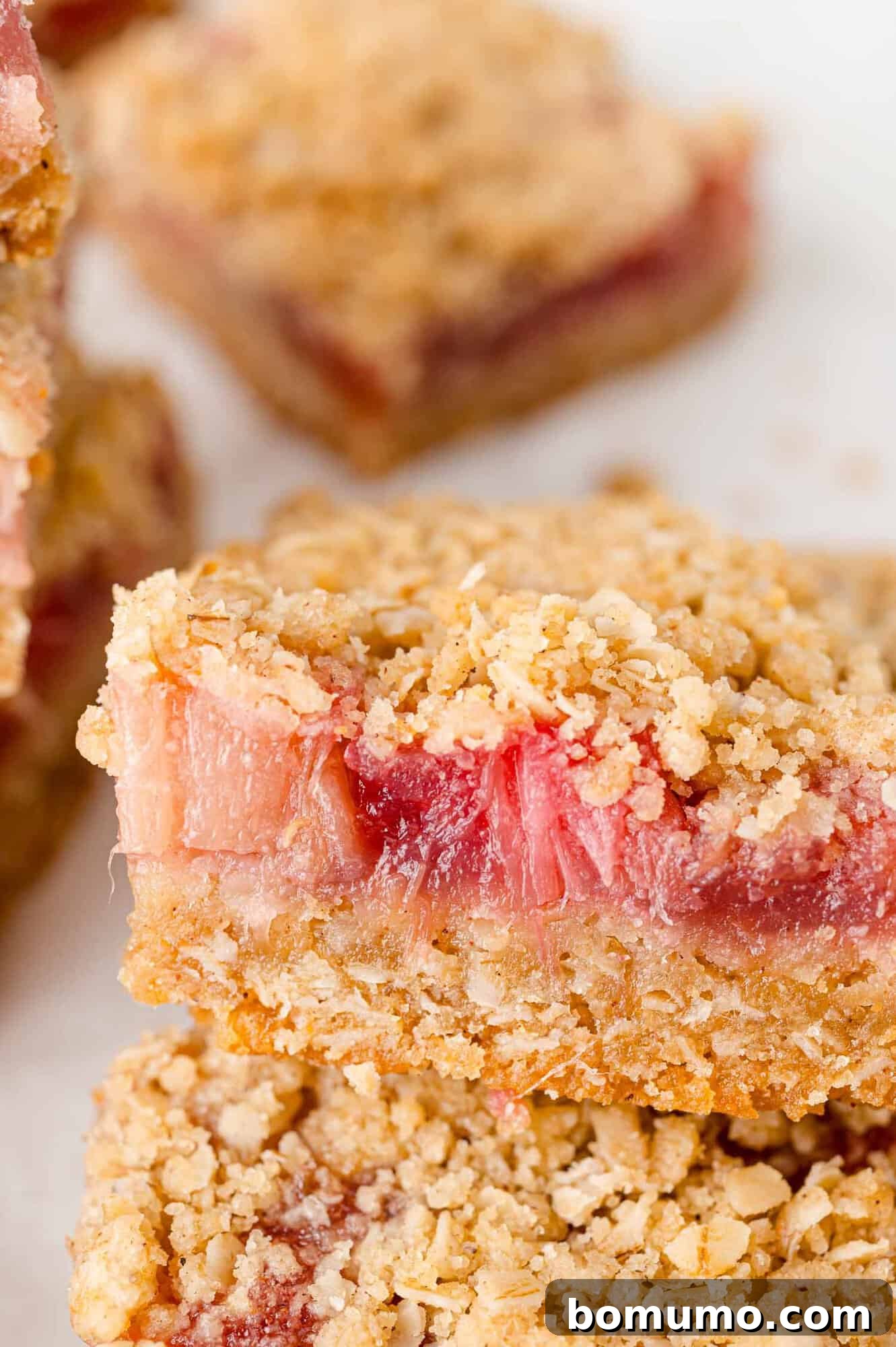 A single rhubarb bar with a crumb topping and a bite taken out, showing the vibrant fruit filling.