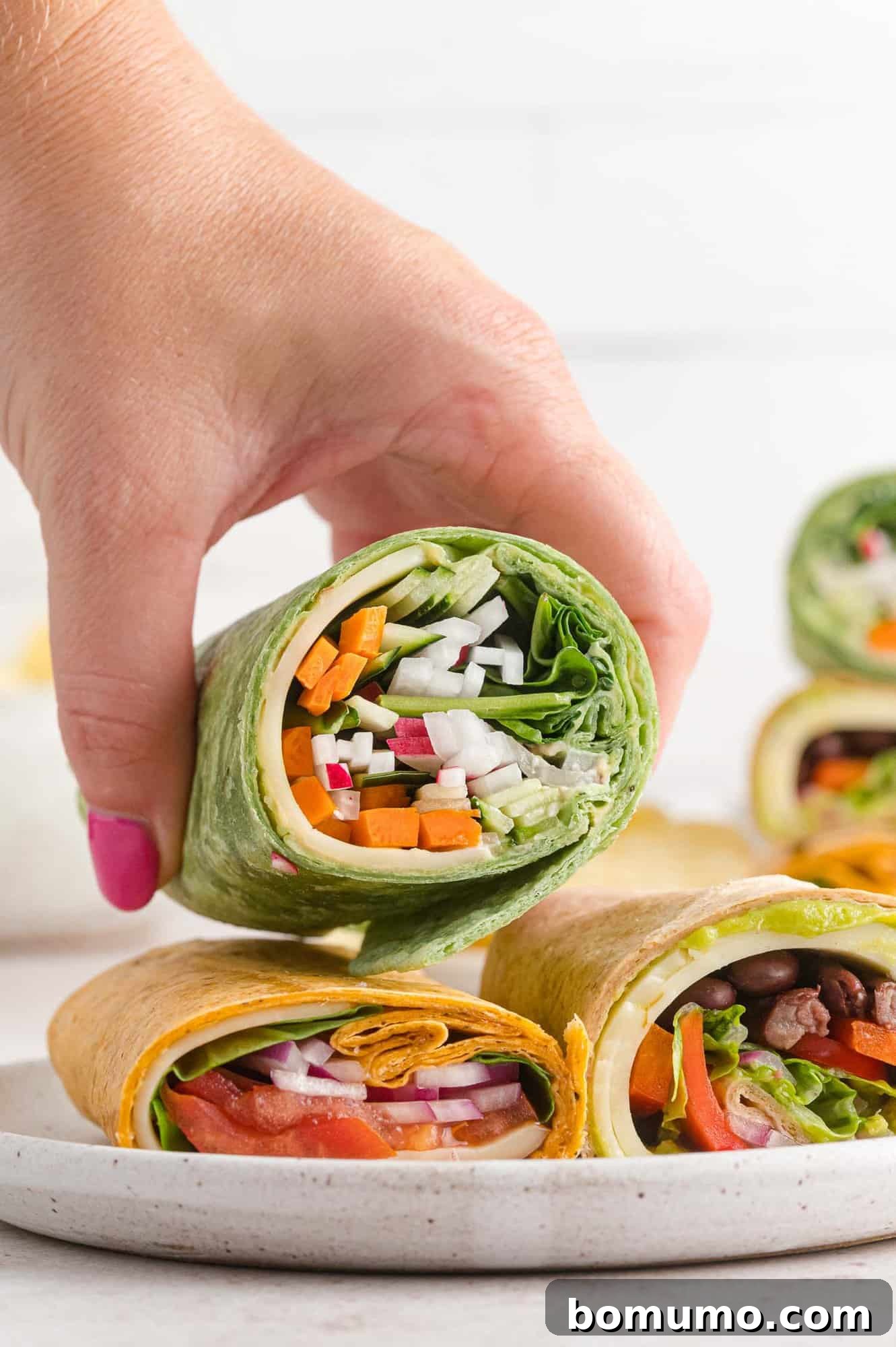 A vibrant veggie wrap, perfectly rolled and held in a hand, showcasing its fresh filling.