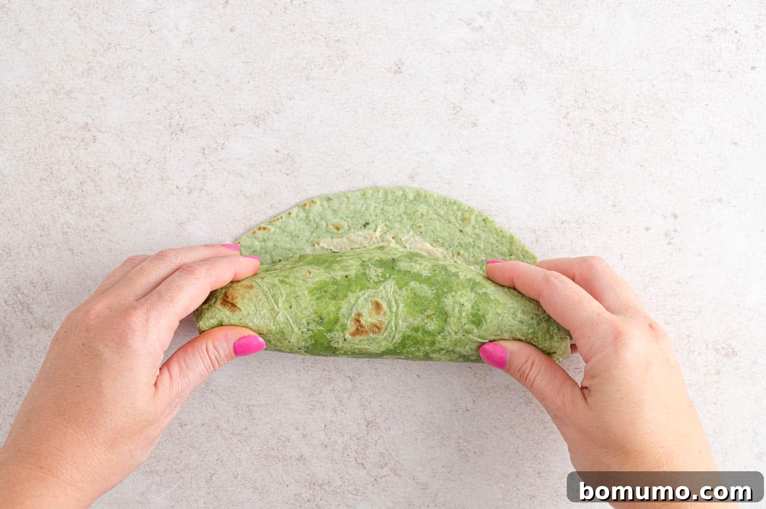 A hand gently rolling a veggie wrap, showcasing the technique to keep the fillings secure.