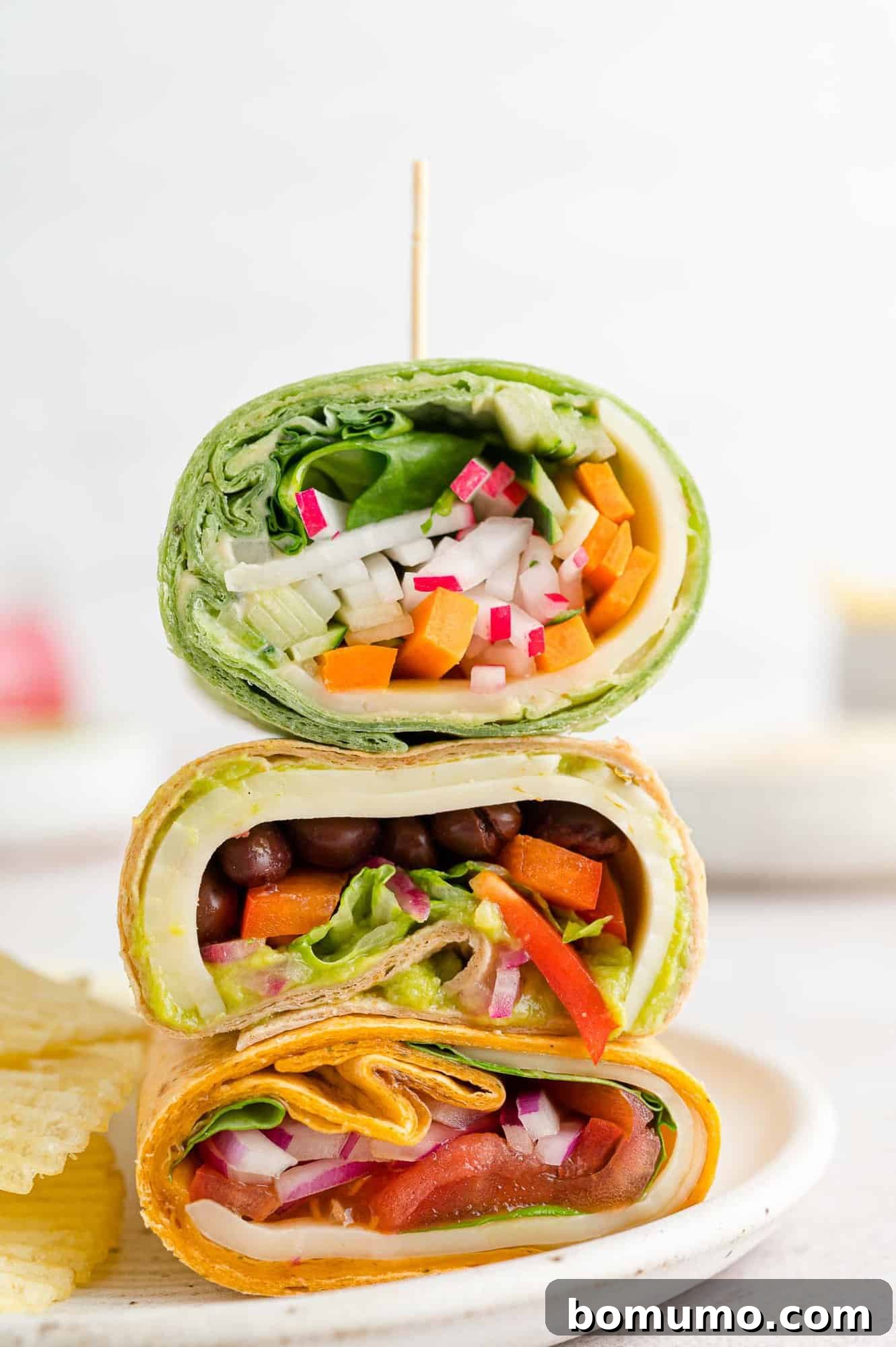 Three colorful veggie wraps, sliced in half and neatly stacked on a white plate, ready to be served.