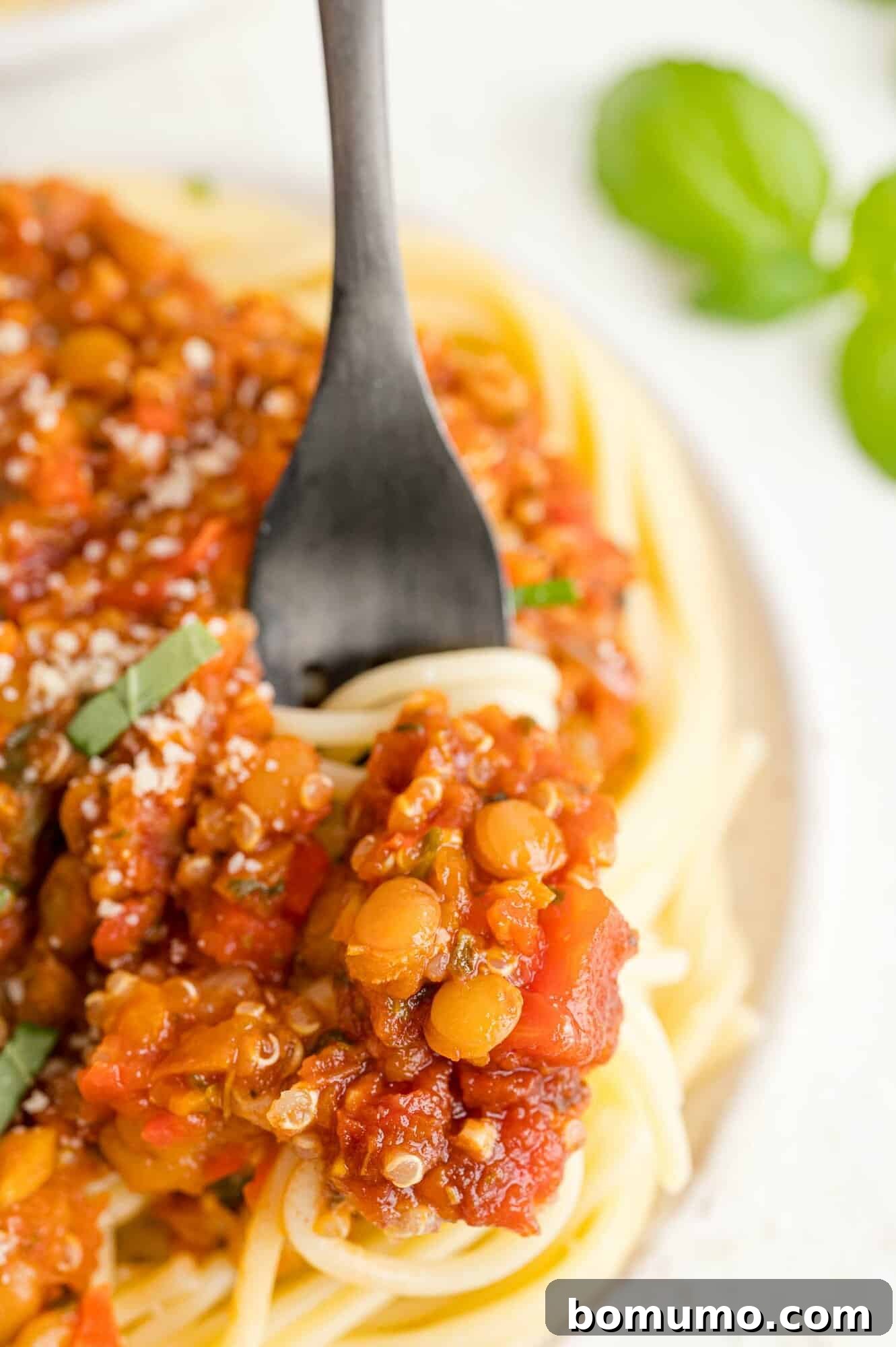 A fork twisting pasta with lentil quinoa bolognese.