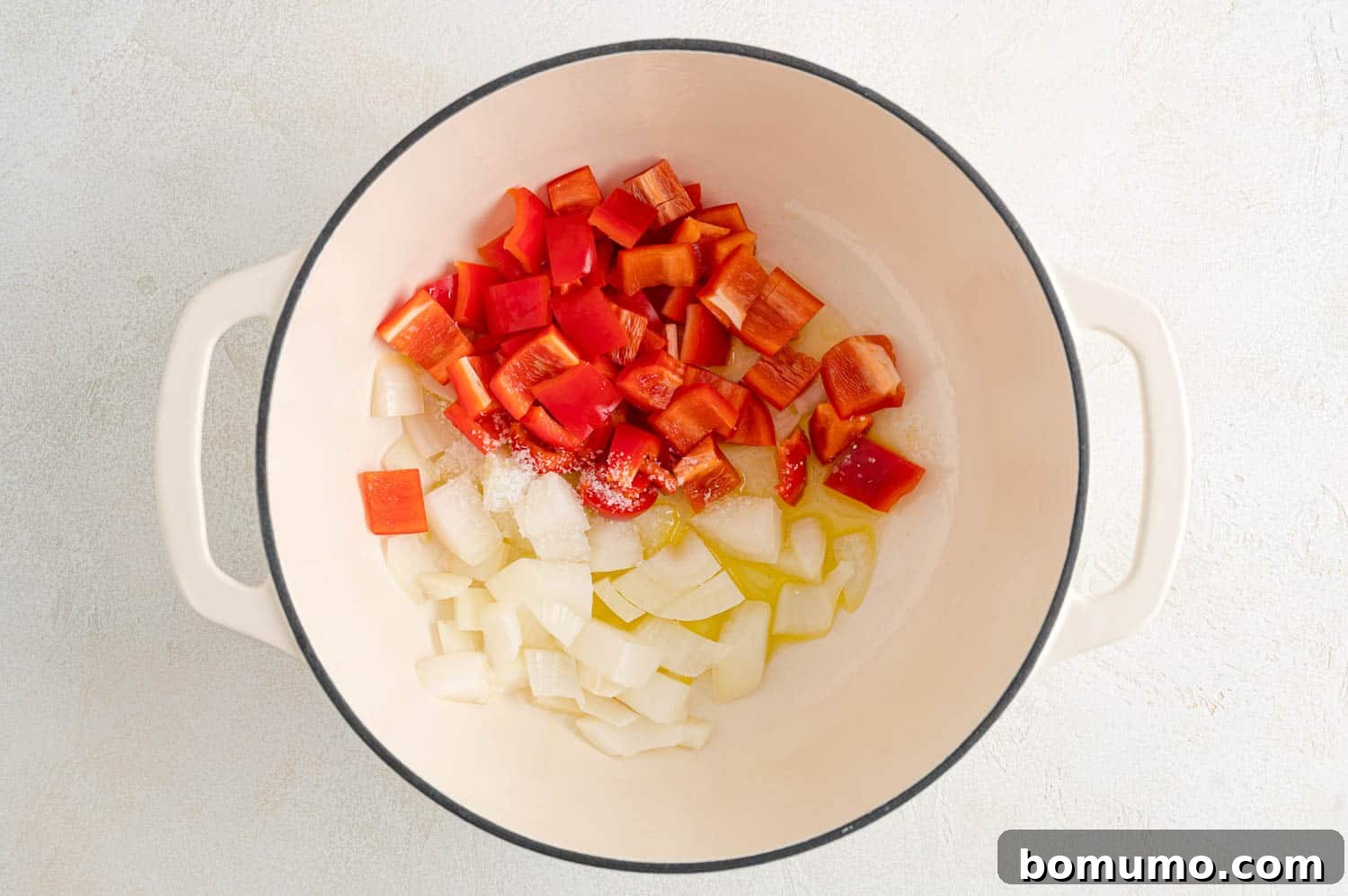 Uncooked peppers and onions sautéing in a pan.
