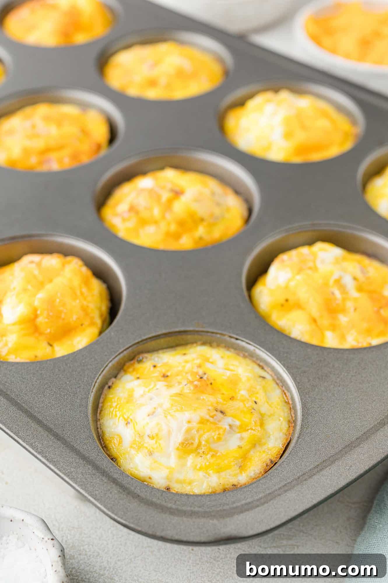 Muffin tin with baked egg muffins topped with melted cheese.