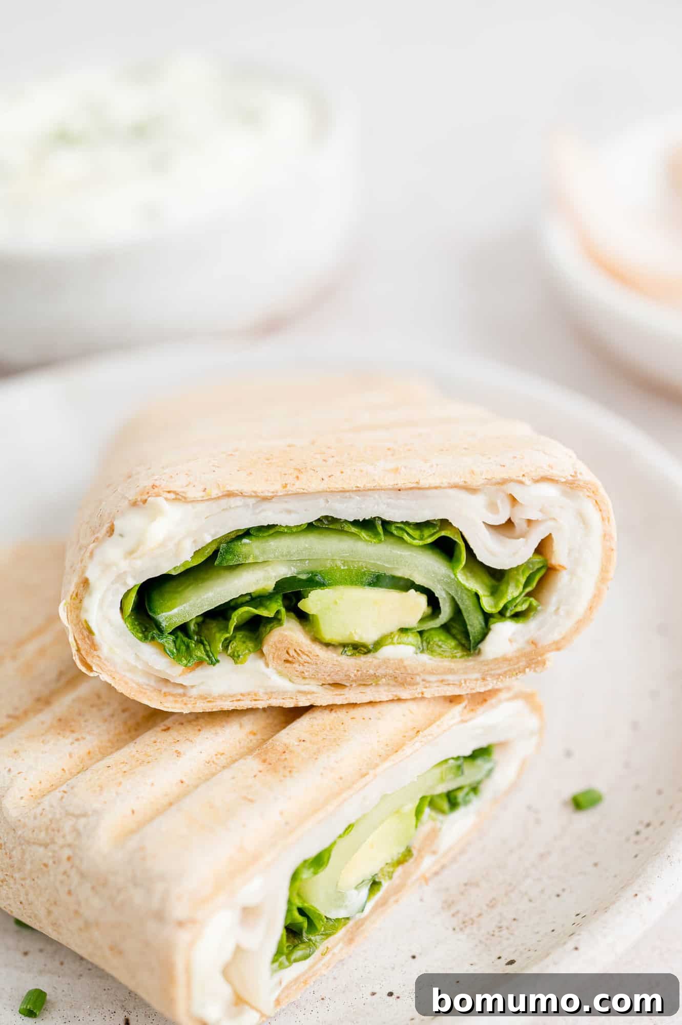 Two meticulously prepared halves of a turkey wrap gracefully resting on a pristine white plate, showcasing its appealing presentation and the fresh, inviting ingredients within.
