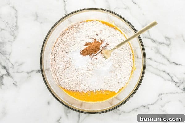 A large mixing bowl containing wet pumpkin mixture, with dry flour and spices resting on top, ready to be incorporated.