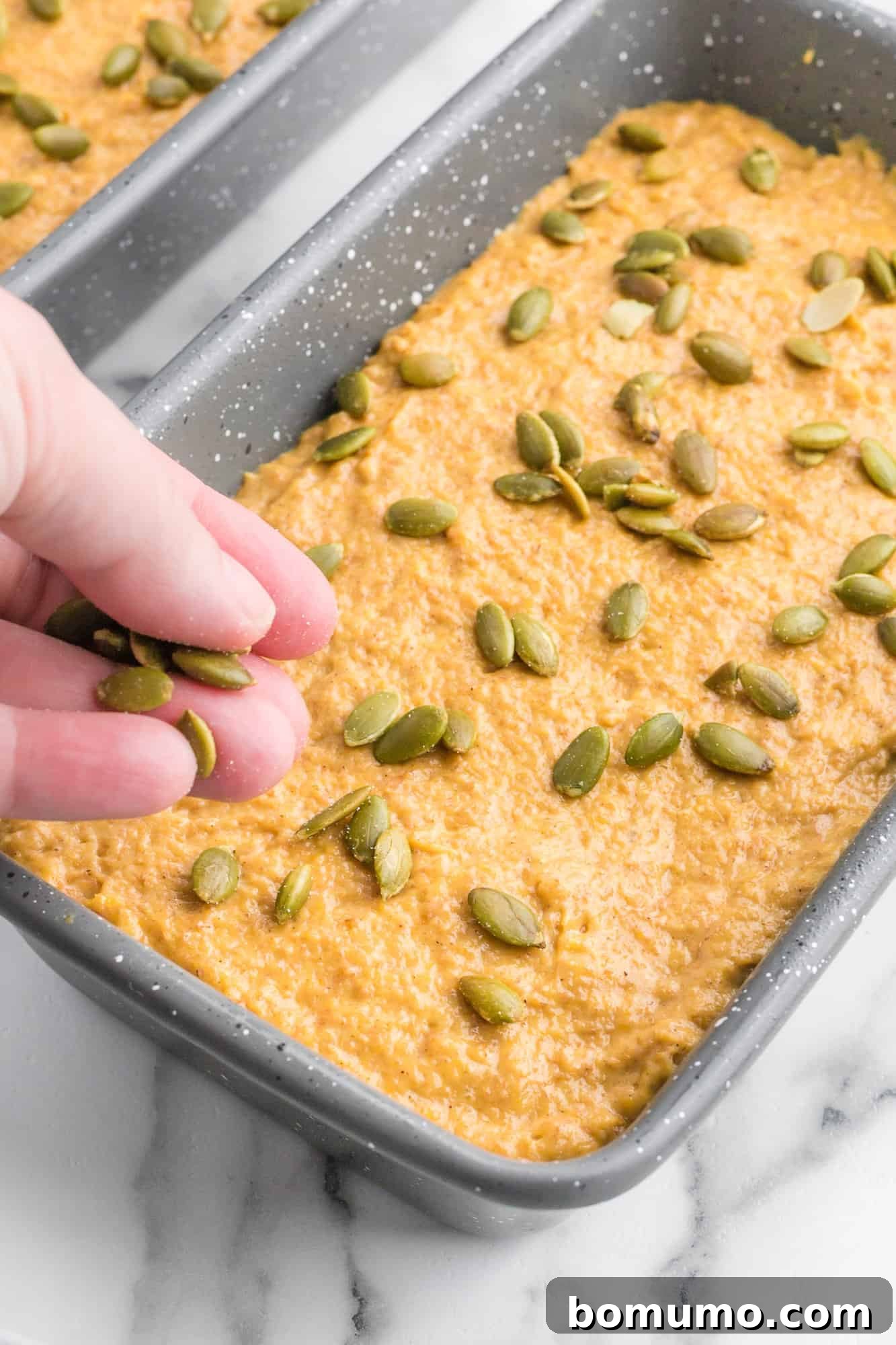 Delicious pumpkin quick bread being sprinkled generously with vibrant green pepitas before baking.