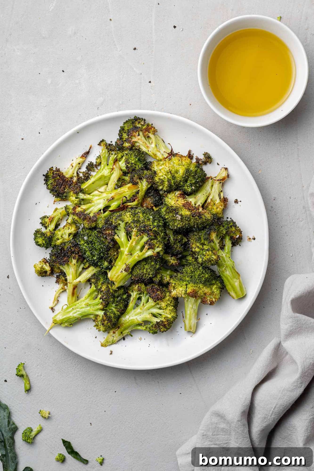 Roasted broccoli in a rustic bowl, with a small bowl of olive oil nearby, ready for serving.