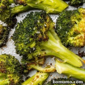 Close up of roasted broccoli floret, surrounded by others, showing crispy edges.