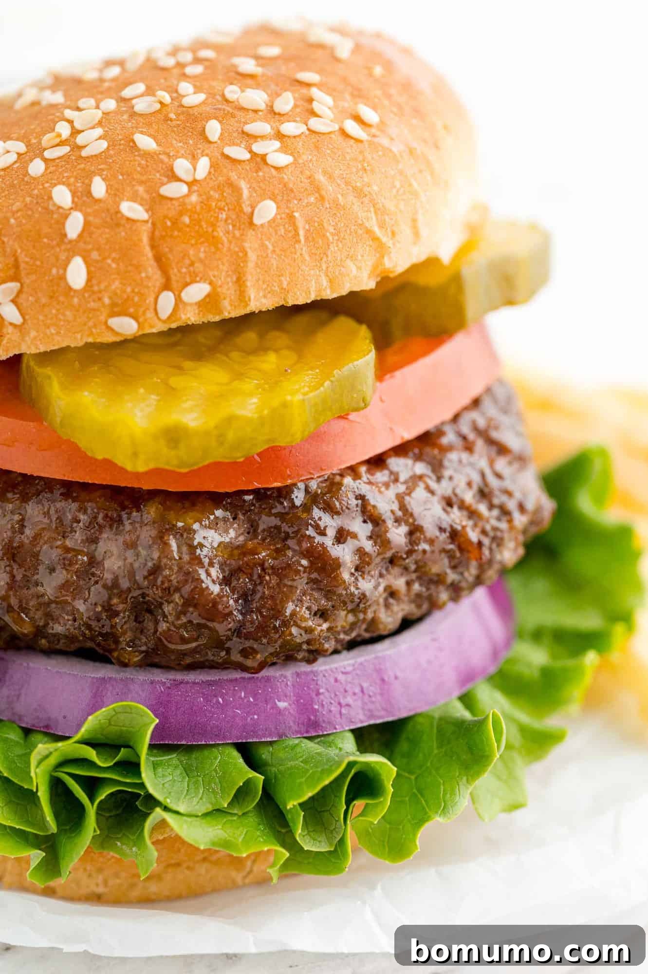 Burger on a sesame seed bun with pickles, tomato, onion, and lettuce.
