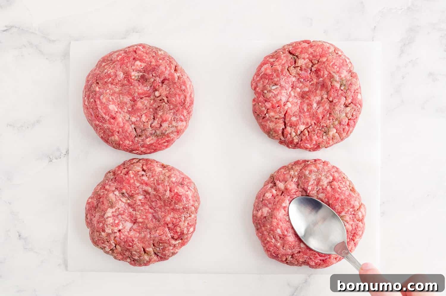 Spoon pressing an indentation in the center of raw burger.