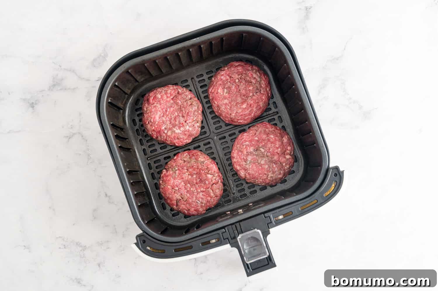 Raw burgers in an air fryer.