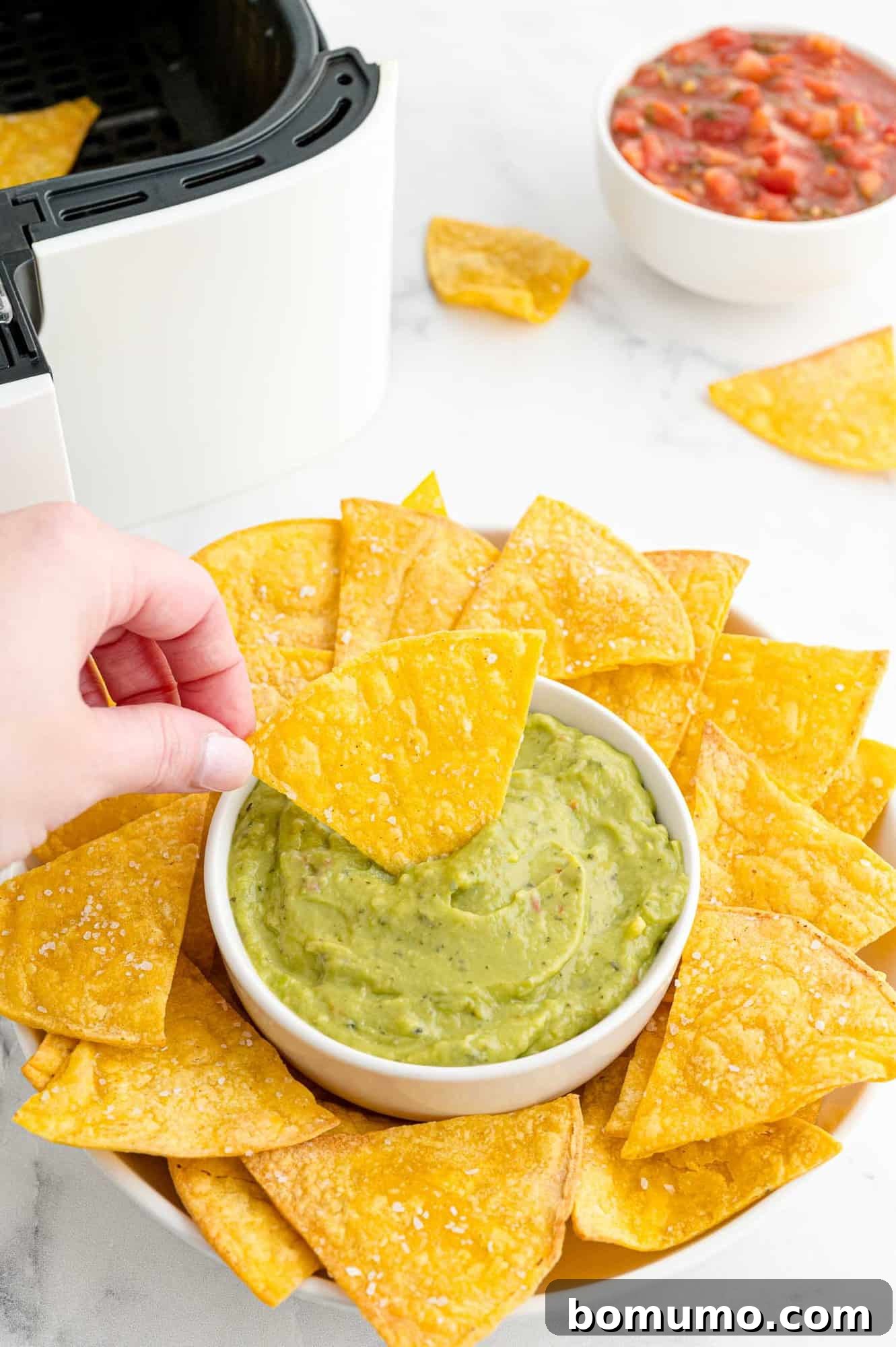 A perfectly air-fried tortilla chip being dipped into a creamy, vibrant green homemade guacamole, ready for a delicious bite.