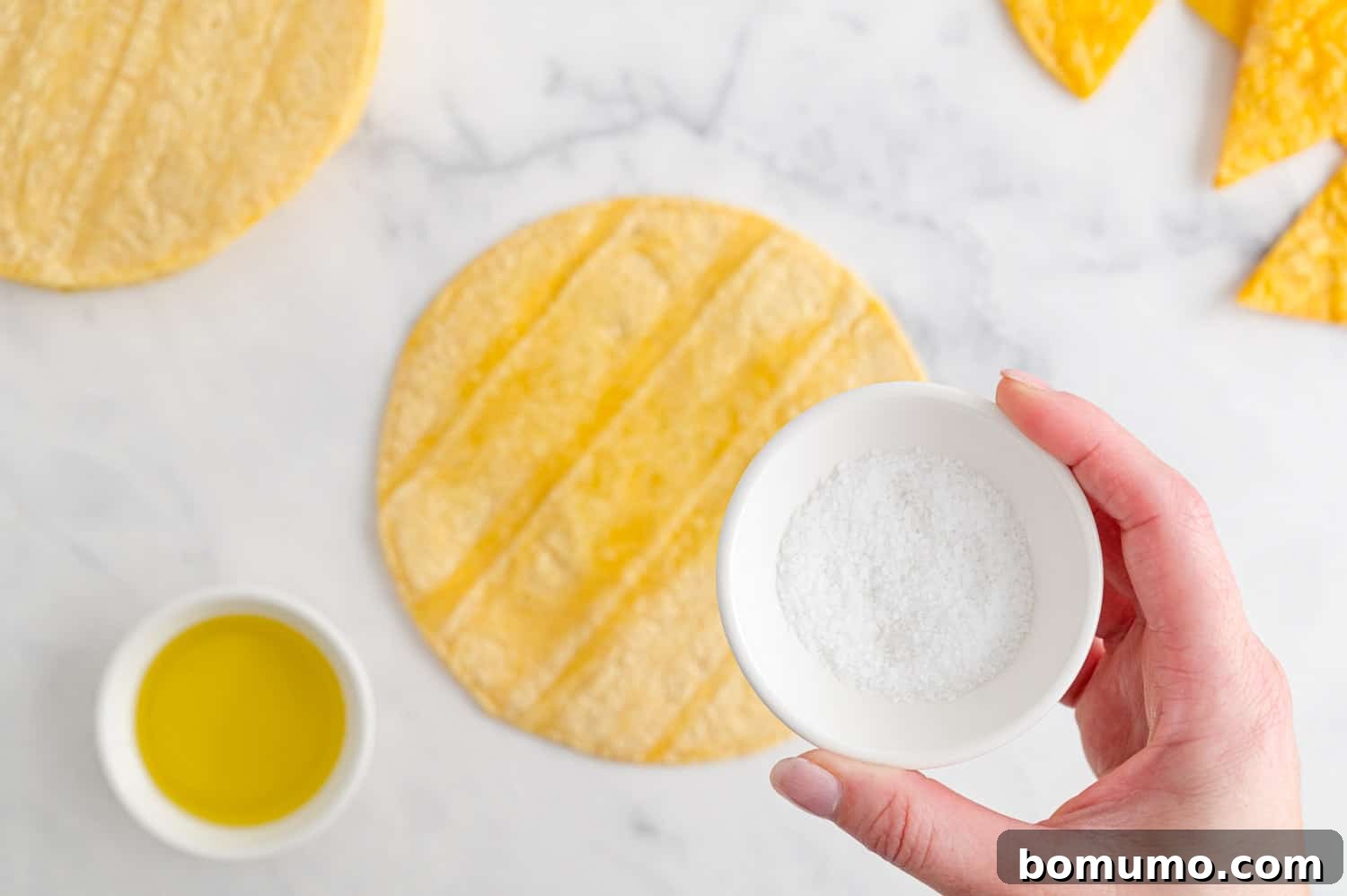 Kosher salt being lightly sprinkled over an oiled corn tortilla, preparing it for slicing and air frying.