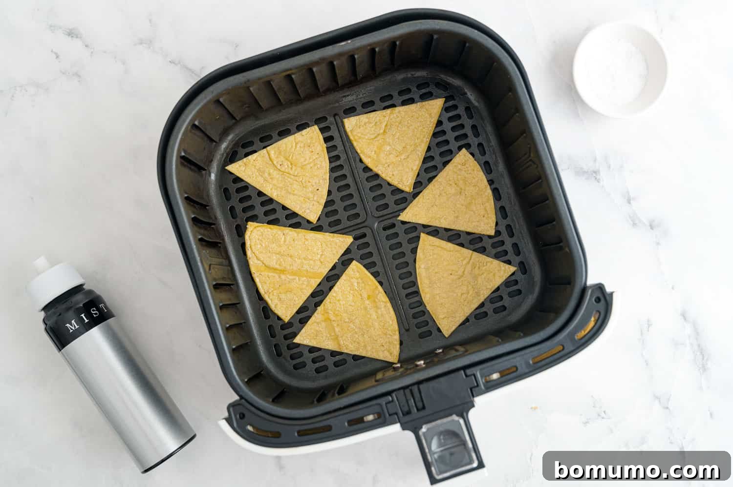 Uncooked, triangular tortilla chip wedges are neatly arranged in a single layer within an air fryer basket, ready for cooking.