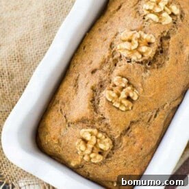 Close up of apple bread topped with walnuts in a white loaf pan.