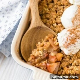 Close up view of apple crisp with ginger, topped with ice cream, being scooped with wooden spoon.
