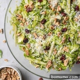 Brussels sprouts salad in a round clear glass bowl, on white marble background.