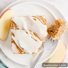 Overhead view of a slice of apple spice cake on a plate with a forkful missing.