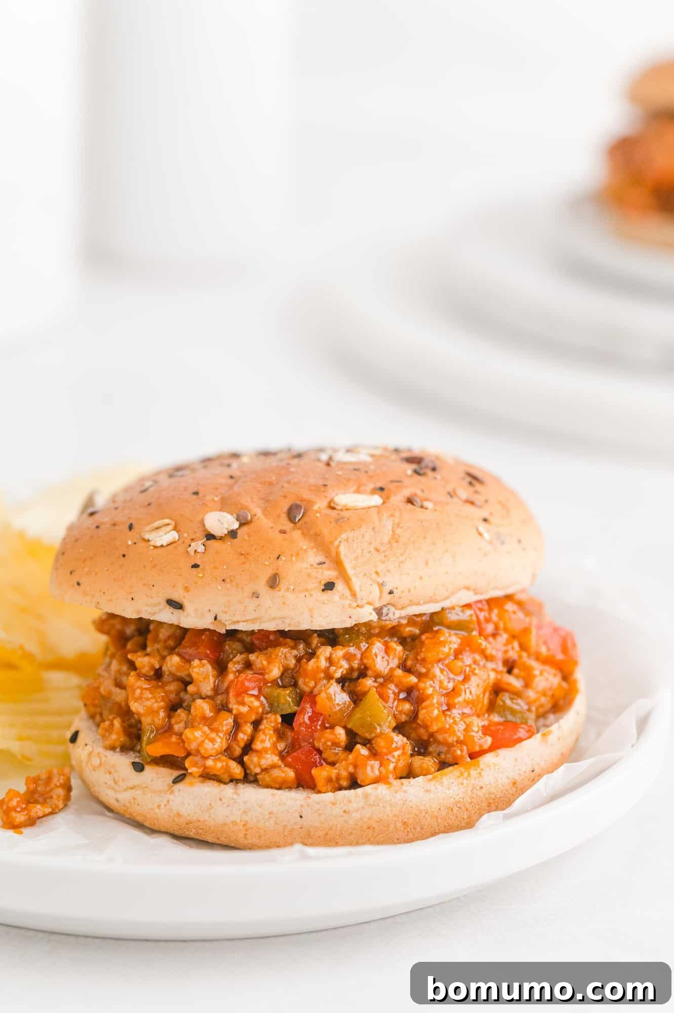 A close-up of a beautifully plated sloppy Joe sandwich on a white plate, adorned with a light garnish, ready to be served as a satisfying dinner.