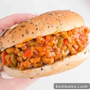 A close-up shot of a hand holding a freshly made sloppy Joe sandwich, showcasing the texture and appeal of the filling.