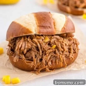 Delectable pulled pork served on a pretzel bun, resting on natural colored parchment paper.