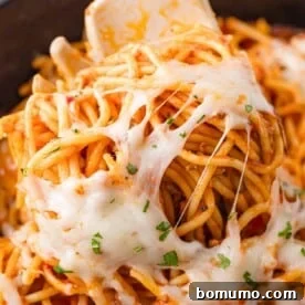 A close-up of delicious Crockpot Spaghetti with melted cheese and fresh herbs, twirled around a fork.