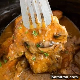 A tender slow cooker pork chop held with tongs, ready to be served.